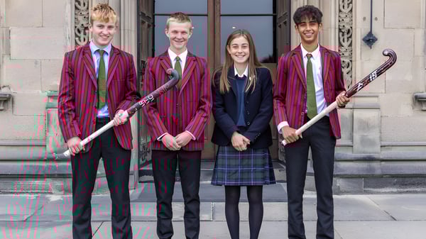 Vier Personen in formeller Kleidung stehen vor einem Gebäude auf dem Campus des Fettes College.