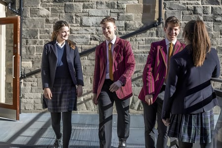 Vier Personen in formeller Kleidung stehen vor einem Steingebäude auf dem Campus des Fettes College.