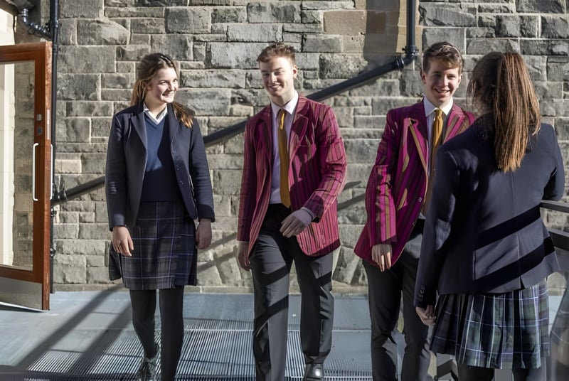 Vier Personen in formeller Kleidung stehen vor einem Steingebäude auf dem Campus des Fettes College.