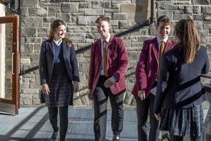 Vier Personen tragen formale Kleidung und stehen vor einem Stein-Gebäude auf dem Campus des Fettes College.