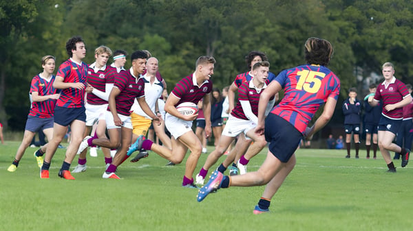 Schüler des Fettes College spielen ein Rugby-Match auf einem grasbewachsenen Spielfeld mit Bäumen im Hintergrund.