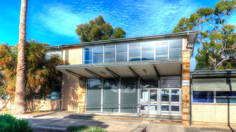 Das moderne Glasgebäude von Findon High School ist von grüner Vegetation umgeben und steht unter klarem blauem Himmel.