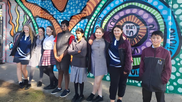 Schülerinnen und Schüler der Findon High School stehen vor einem farbenfrohen Wandbild mit geometrischen Mustern.