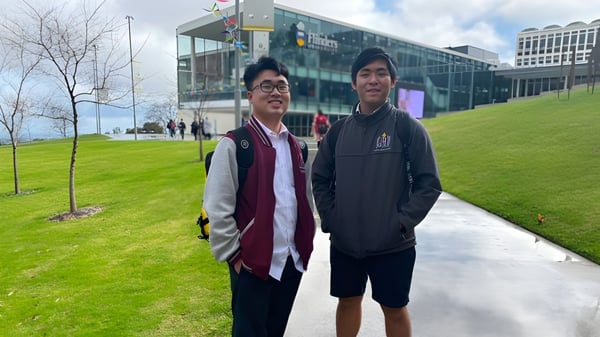Zwei Schüler stehen vor einem modernen Gebäude auf dem Campus der Findon High School mit einer Rasenfläche im Hintergrund.
