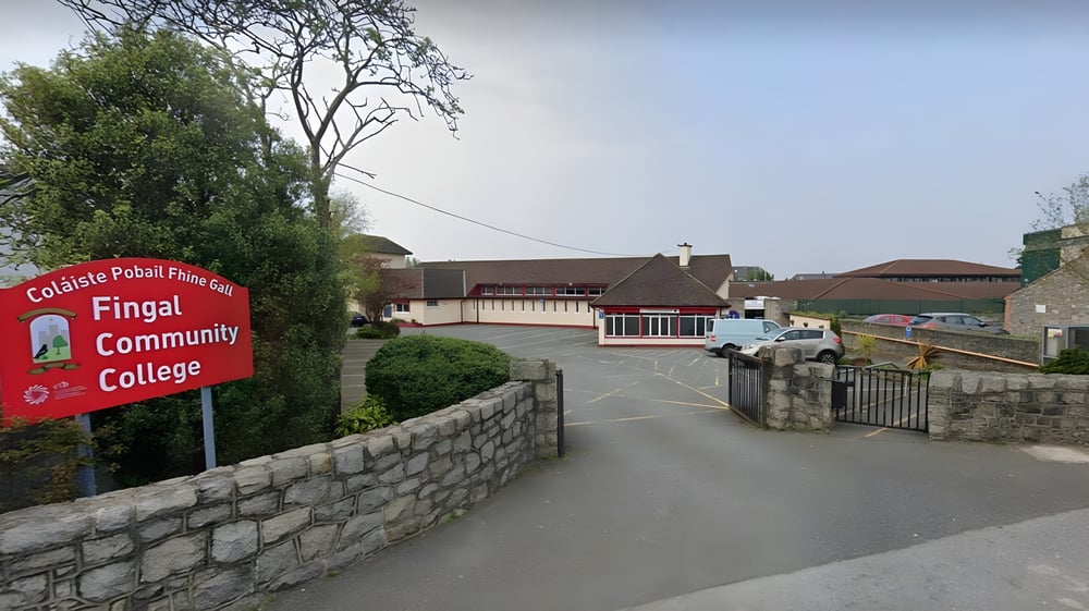 Ein rotes Schild des Fingal Community College steht vor einer Steinmauer mit Gebäuden im Hintergrund.