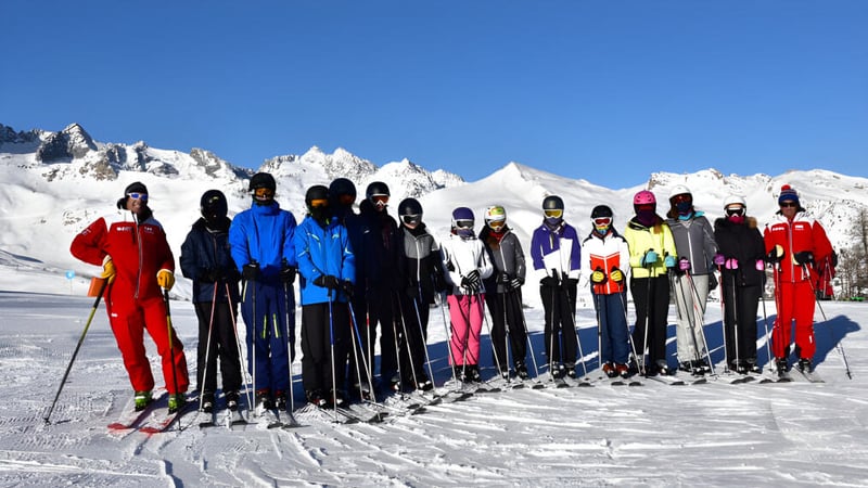 Schüler der Firrhill High School stehen in bunter Kleidung auf einem schneebedeckten Abhang mit schneebedeckten Bergen im Hintergrund.