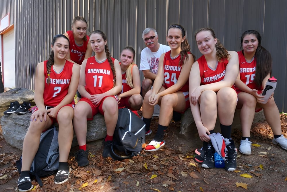 Eine Gruppe von Schülerinnen und Schülern der FJ Brennan Catholic High School sitzt auf dem Boden umgeben von Herbstlaub.
