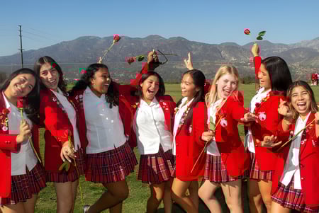 Schülerinnen der Flintridge Sacred Heart Academy feiern in roten und weißen Abschlussroben vor einer Berglandschaft.