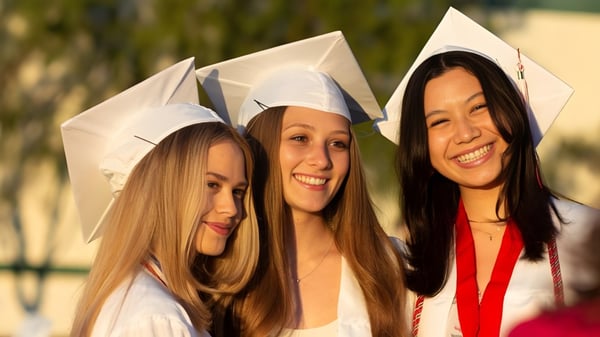 Drei Schülerinnen der Flintridge Sacred Heart Academy in Abschlusskleidung stehen gemeinsam draußen vor natürlichem Hintergrund.