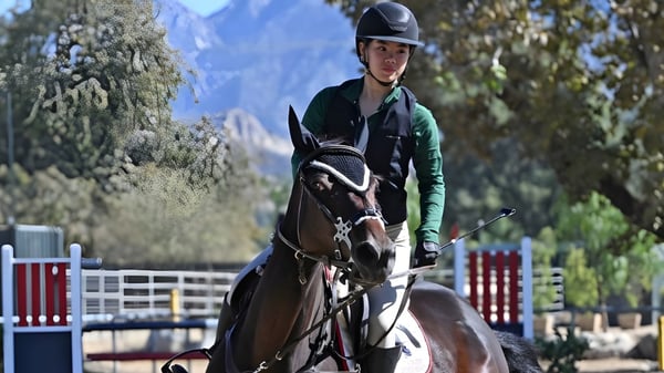 Eine Schülerin der Flintridge Sacred Heart Academy reitet ein Pferd im Freien vor Bäumen und Bergen.