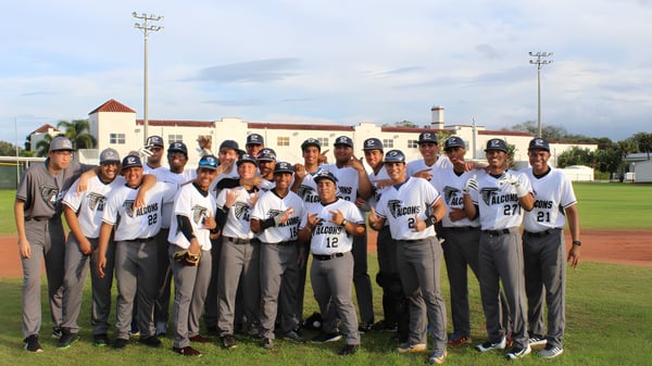 Eine Gruppe von Baseballspielerinnen und Baseballspielern der Florida Preparatory Academy steht auf dem Baseballfeld vor einem Gebäude mit Sportbeleuchtung.