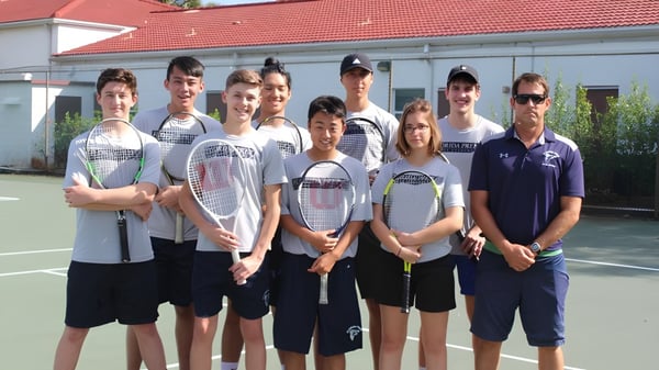 Die Tennisgruppe der Florida Preparatory Academy posiert gemeinsam auf dem Tennisplatz vor einem Schulgebäude.