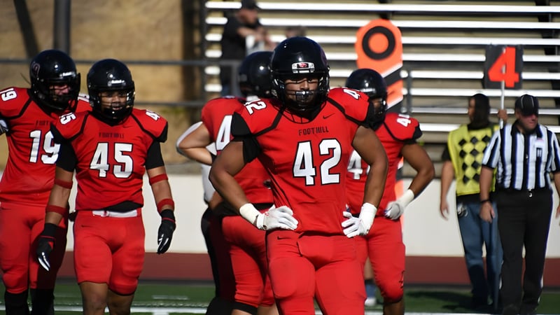Eine Gruppe von Football-Spielern in roten Uniformen spielt auf dem Feld des Foothill College mit Schiedsrichter im Hintergrund.