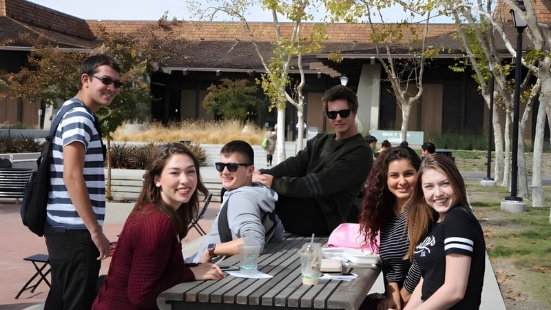 Eine Gruppe Schüler versammelt sich auf einem Holzdeck vor einem rustikalen Gebäude auf dem Campus des Foothill College.