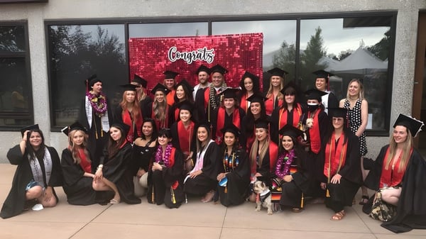 Eine große Gruppe von vorwiegend jungen Frauen steht vor einem roten Foothill College Hintergrund mit der Aufschrift 'Congrats'.