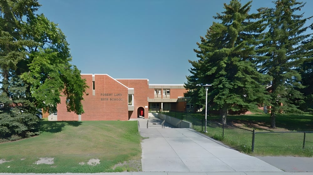 Das Backsteingebäude der Forest Lawn High School mit rotem Dach steht umgeben von grünen Bäumen unter blauem Himmel.
