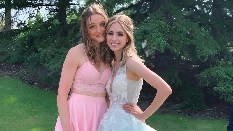 Zwei Schülerinnen der Forest Lawn High School umarmen sich lächelnd im grünen Außenbereich mit Bäumen im Hintergrund.