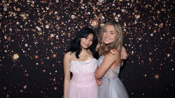 Zwei Schülerinnen der Forest Ridge School of the Sacred Heart stehen gemeinsam vor funkelnden Lichtern bei einer festlichen Veranstaltung.