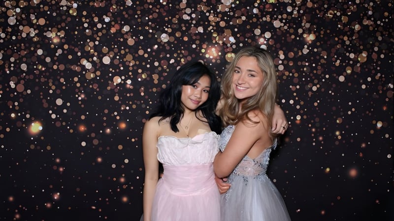 Zwei Schülerinnen der Forest Ridge School of the Sacred Heart stehen gemeinsam vor funkelnden Lichtern bei einer festlichen Veranstaltung.