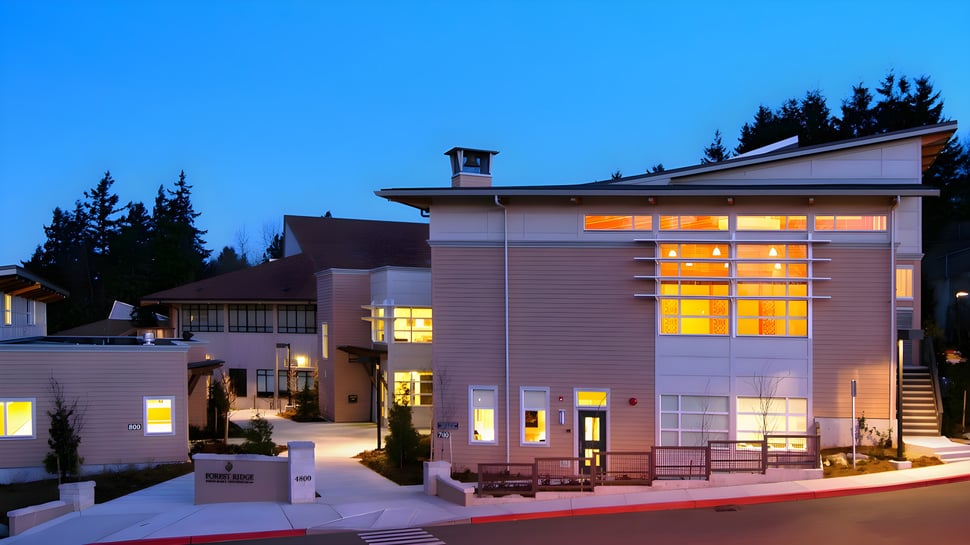 Das mehrstöckige Gebäude der Forest Ridge School of the Sacred Heart steht bei Nacht mit beleuchteten Fenstern umgeben von Bäumen.