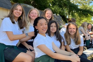 Eine Gruppe lächelnder Schülerinnen steht draußen auf dem Gelände der Forest Ridge School of the Sacred Heart vor grüner Vegetation.