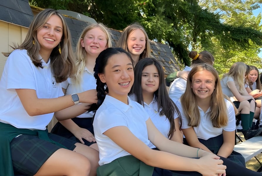 Eine Gruppe lächelnder Schülerinnen steht draußen auf dem Gelände der Forest Ridge School of the Sacred Heart vor grüner Vegetation.