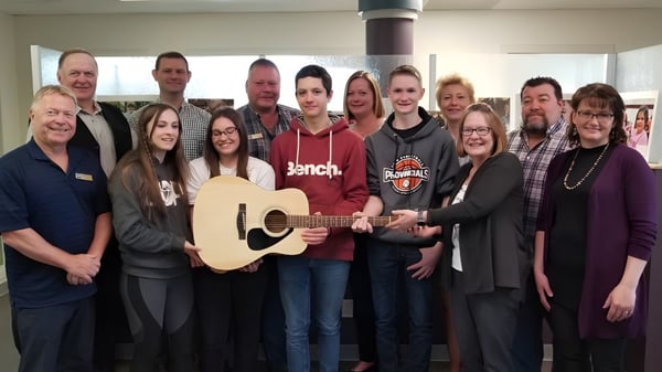 Eine Gruppe von Schülern der Forestburg School musiziert gemeinsam in einem Innenraum mit einem Gitarrenspieler in der Mitte.