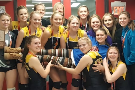 Eine Gruppe junger Schülerinnen der Forestburg School versammelt sich lächelnd in einer Sporthalle.