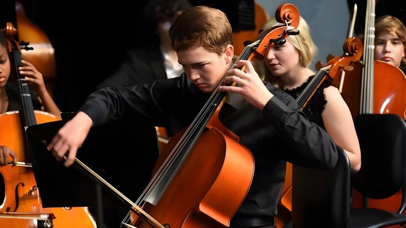 Ein Schüler der Forsyth Country Day School spielt konzentriert Cello auf einer Bühne mit anderen Streichinstrumentmusikern.