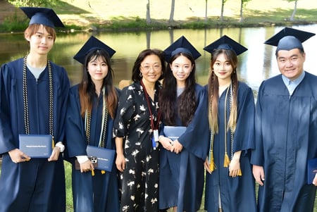 Eine Gruppe von Absolventen der Forsyth Country Day School steht in akademischer Kleidung vor einer landschaftlichen Kulisse mit Wasser.