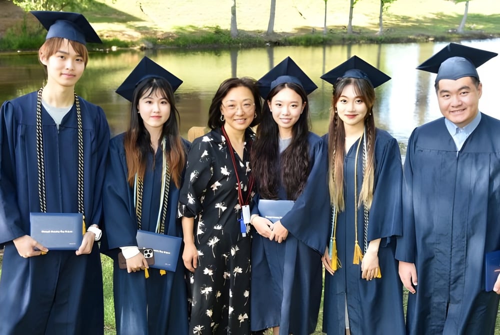 Eine Gruppe von Absolventen der Forsyth Country Day School steht in akademischer Kleidung vor einer landschaftlichen Kulisse mit Wasser.