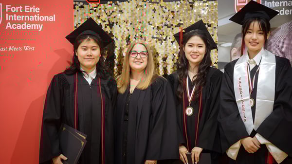 Eine Gruppe von Absolventinnen und Absolventen der Fort Erie International Academy posiert in akademischer Kleidung vor einem Banner mit dem Namen der Schule.