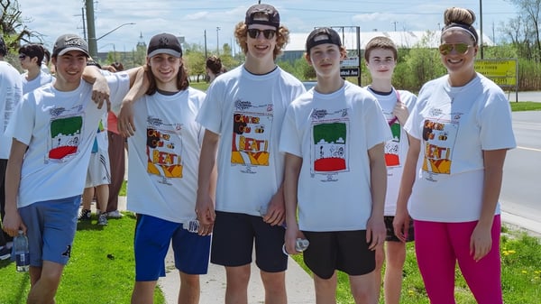 Eine Gruppe Schülerinnen und Schüler der Fort Erie International Academy steht gemeinsam im Freien auf einer Wiese mit Bäumen im Hintergrund.