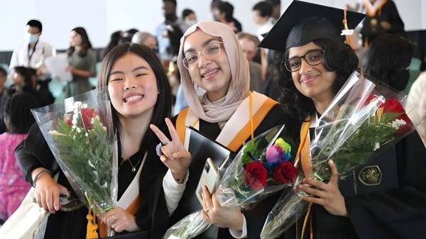 Eine Gruppe von Absolventinnen in Abschlusskleidung mit Blumen steht auf dem Gelände der Fort Richmond Collegiate.