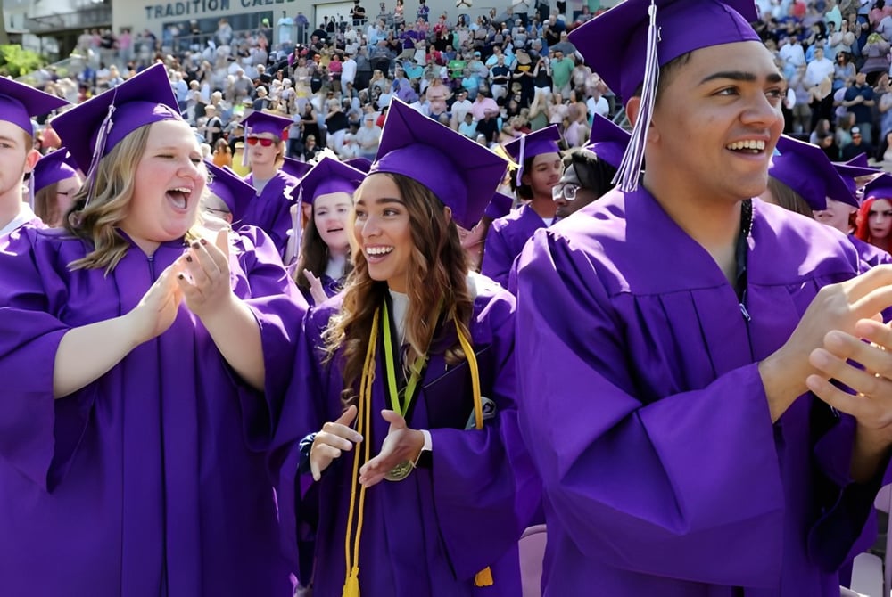 Absolventinnen und Absolventen der Fort St. James Secondary feiern im Freien ihren Abschluss in lila Talaren.