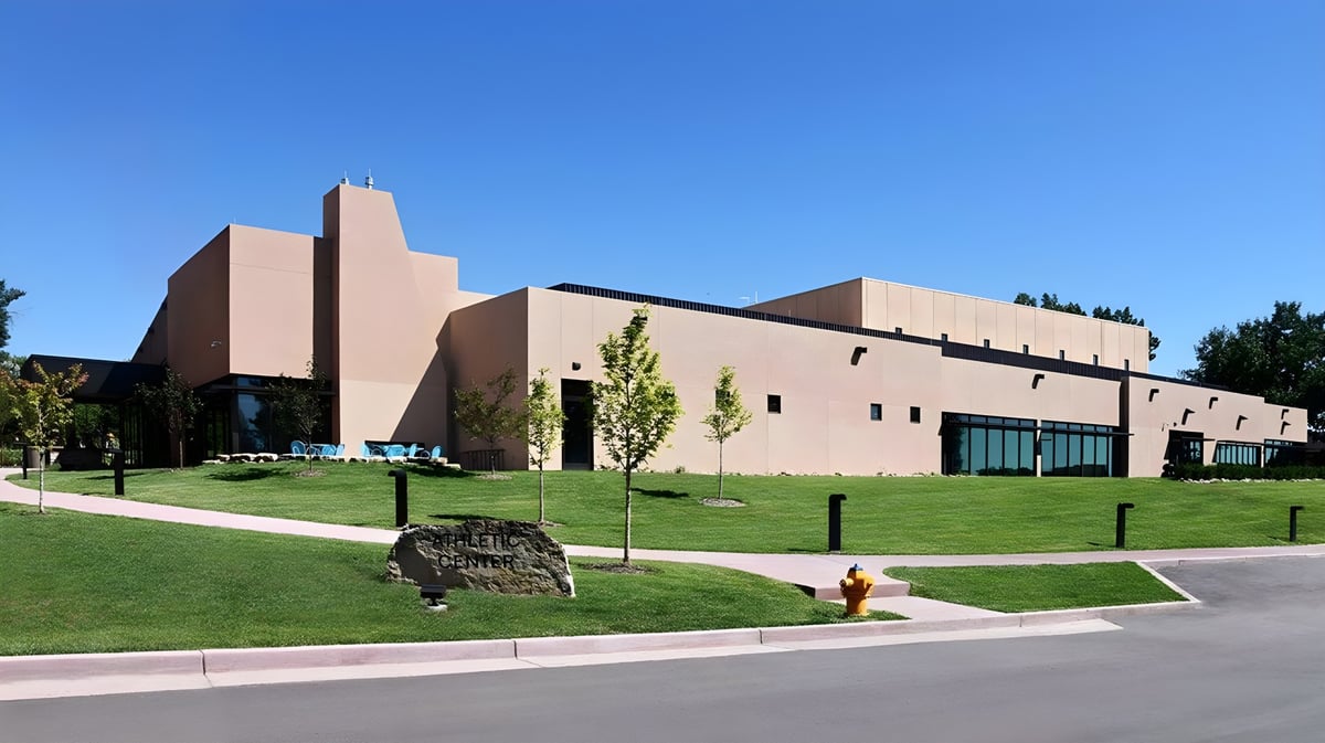 Das moderne mehrstöckige Gebäude der Fountain Valley School of Colorado steht auf einem gepflegten Rasen mit Bäumen und blauem Himmel.