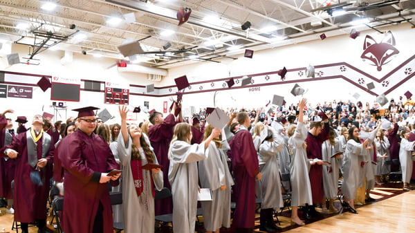 Eine große Gruppe von Schülern der Fox Valley Lutheran High School steht in ihren Abschlussroben in einer geschmückten Halle.