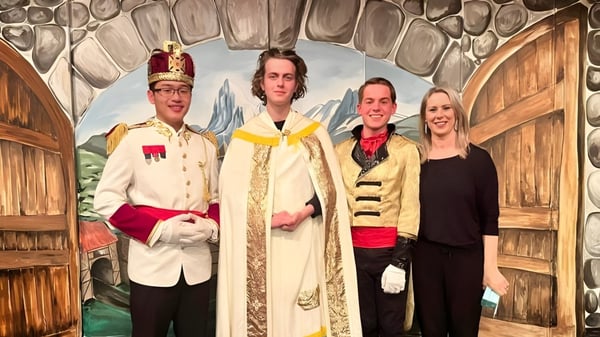 Vier Schülerinnen und Schüler des Francis Douglas Memorial College stehen in farbenfrohen Kostümen vor einer rustikalen Holzkulisse.