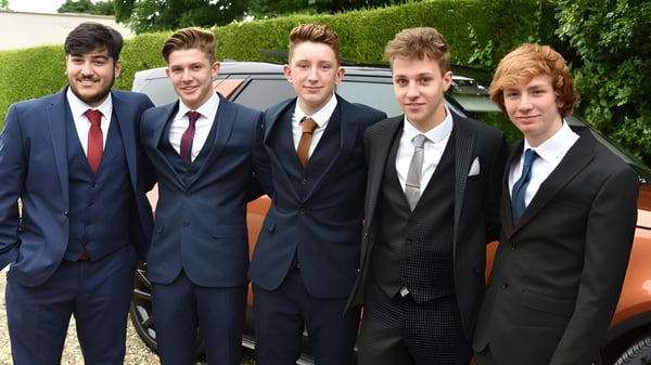 Schüler des Franciscan College Gormanston stehen in formeller Kleidung vor einem Auto umgeben von grüner Vegetation.