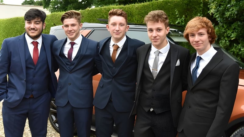 Schüler des Franciscan College Gormanston stehen in formeller Kleidung vor einem Auto umgeben von grüner Vegetation.