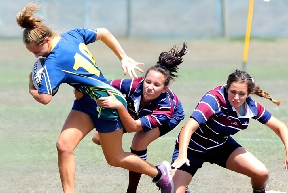 Drei Schülerinnen des Fraser Coast Anglican College nehmen an einem sportlichen Wettkampf auf einem Grasfeld teil.