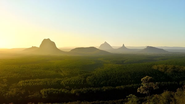 Eine grüne Landschaft mit hohen, gezackten Bergen bei Sonnenuntergang nahe dem Fraser Coast Anglican College.