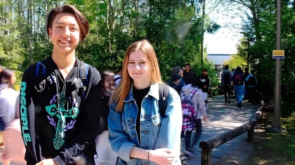 Zwei Schülerinnen stehen draußen auf dem Campus der Fraser Heights Secondary School vor Bäumen und einer Menschenmenge.