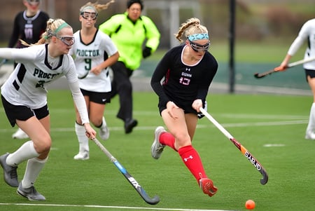 Schüler der Frederick Gunn School spielen ein Feldhockeyspiel auf dem Kunstrasen mit Zuschauern und Trainern im Hintergrund.