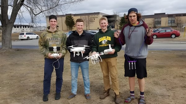 Eine Gruppe Schülerinnen und Schüler steht auf einer Wiese vor Gebäuden auf dem Campus der Fredericton High School.