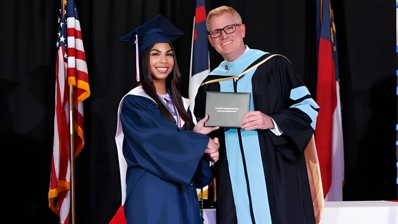 Eine Absolventin der Freedom Christian Academy schüttelt nach der Abschlussfeier einem Mann in akademischer Robe die Hand.