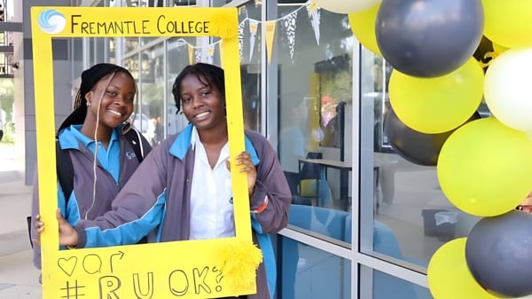 Zwei schuelerinnen stehen vor einem Fremantle College Schild mit bunten Ballons im Hintergrund.