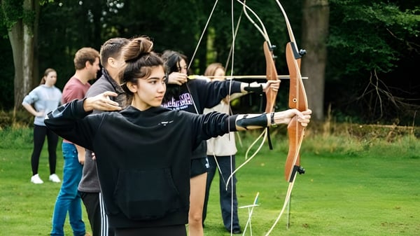 Schüler der Frensham Heights School üben Bogenschießen auf einem grasbewachsenen Feld mit Bäumen im Hintergrund.