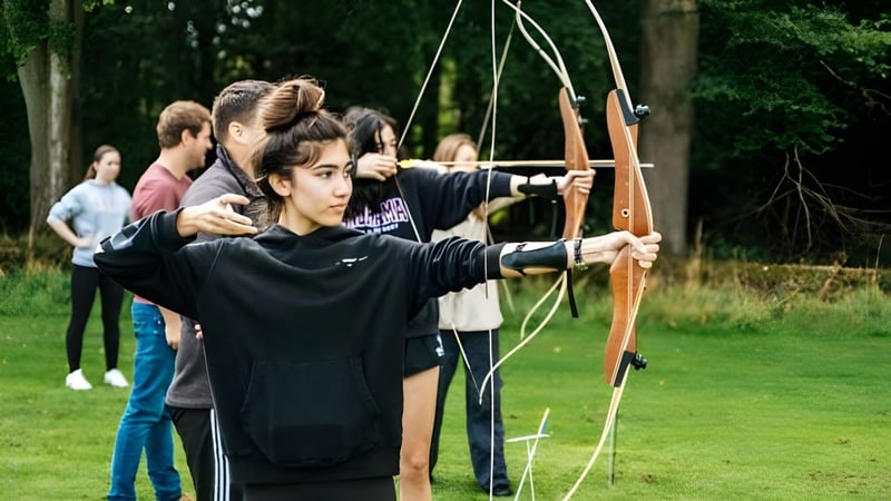 Schüler der Frensham Heights School üben Bogenschießen auf einem grasbewachsenen Feld mit Bäumen im Hintergrund.