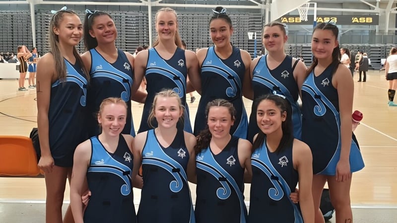 Eine Gruppe junger Schülerinnen in Sportuniformen posiert gemeinsam auf dem Basketballplatz der Freyberg High School.